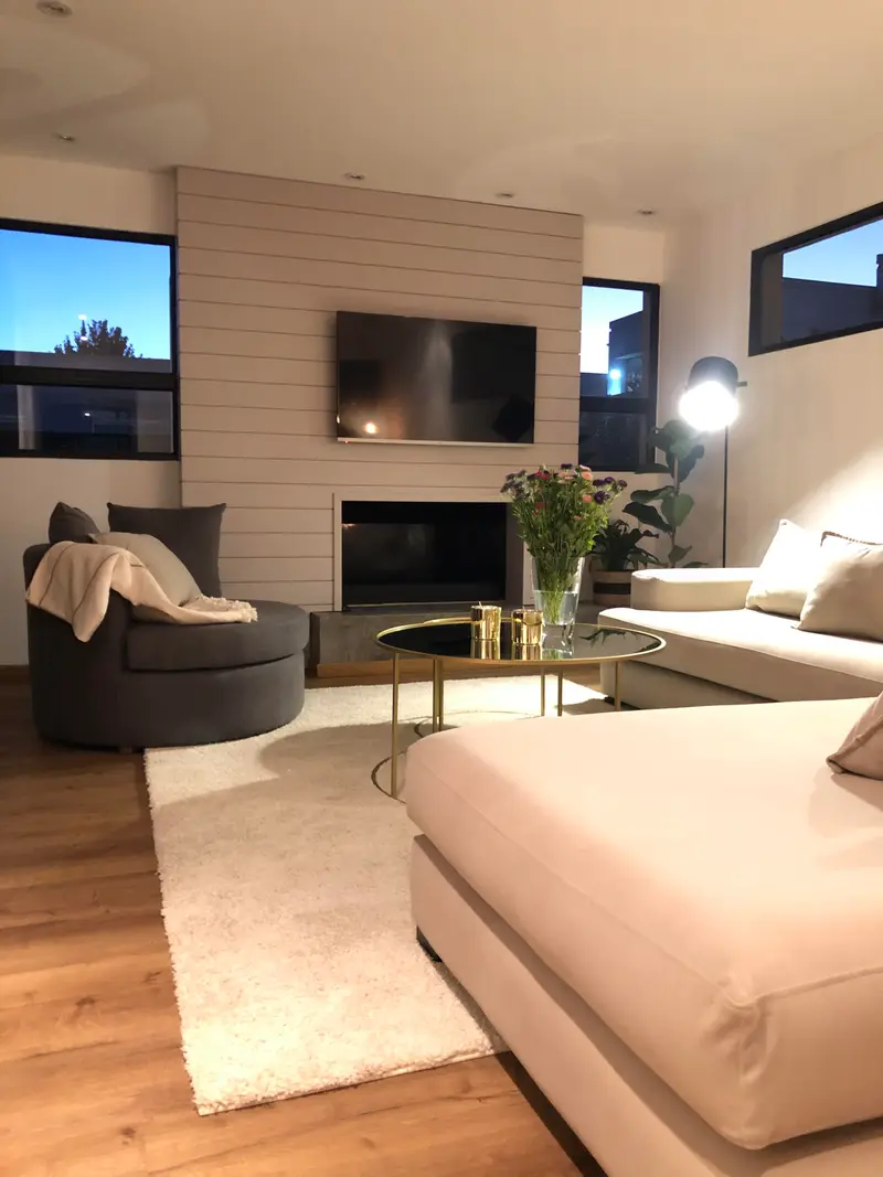 Living con un sillón curvo, sofás claros, revestimiento de madera y una chimenea.