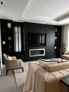 Living con sillones claros, mesa de centro y pared de televisión negra con estantes laterales.