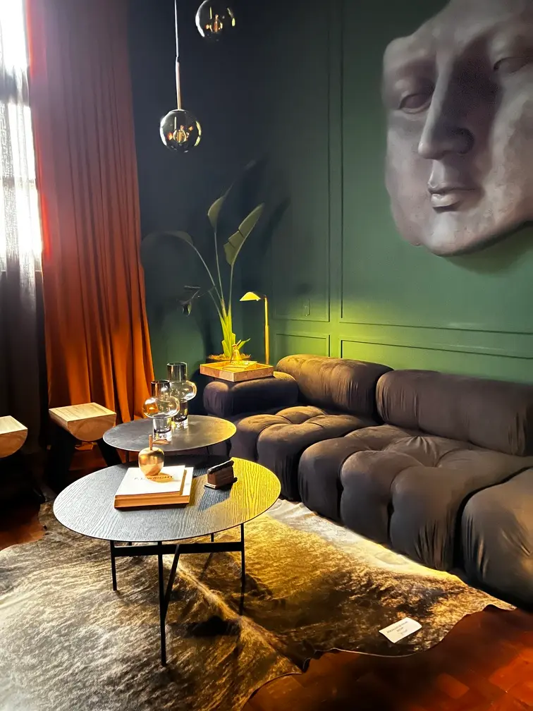 Living con sillón gris, pared verde, escultura de un rostro y mesas auxiliares de distintos materiales.