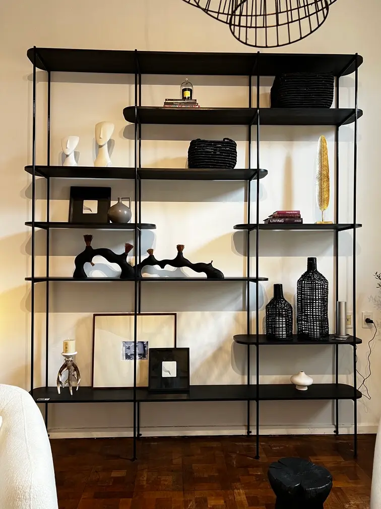 Biblioteca abierta de estructura negra y estantes de madera, con libros y objetos decorativos.